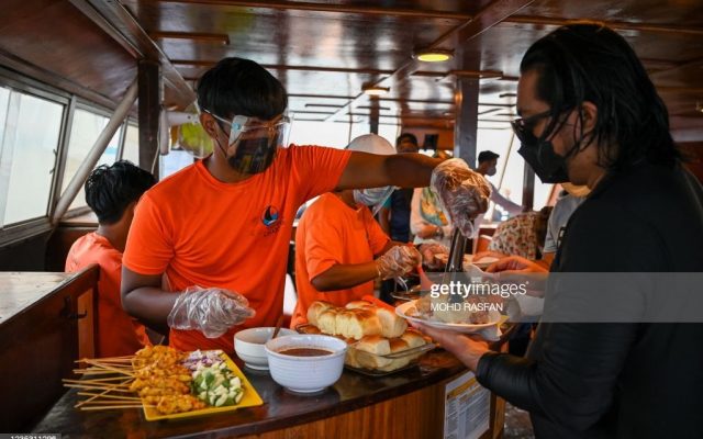 Workers serve dinner to passengers onboard a catamaran yacht in Langkawi on September 17, 2021, as the holiday island reopened to domestic tourists following closures due to Covid-19 restrictions. (Photo by Mohd RASFAN / AFP) (Photo by MOHD RASFAN/AFP via Getty Images)